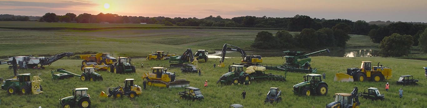 אנשים צועדים בין ציוד שונה של John Deere בשדה גדול.