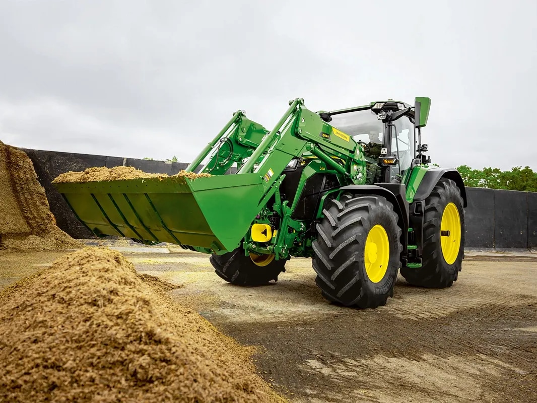 כף מעמיס קדמי מלאה במספוא בטרקטור John Deere במהלך עבודת טיפול בחומר.
