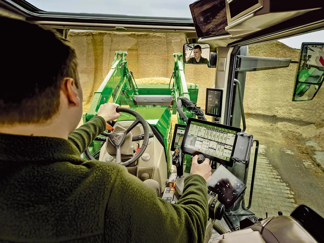 מבט מבפנים על התא של טרקטור John Deere עם בקרות המפעיל והפעלת המעמיס הקדמי.