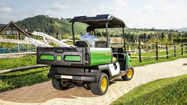 מבט מאחור על John Deere Gator GS שנוסע בשביל לבנים עם גבעות וכרמים ברקע.
