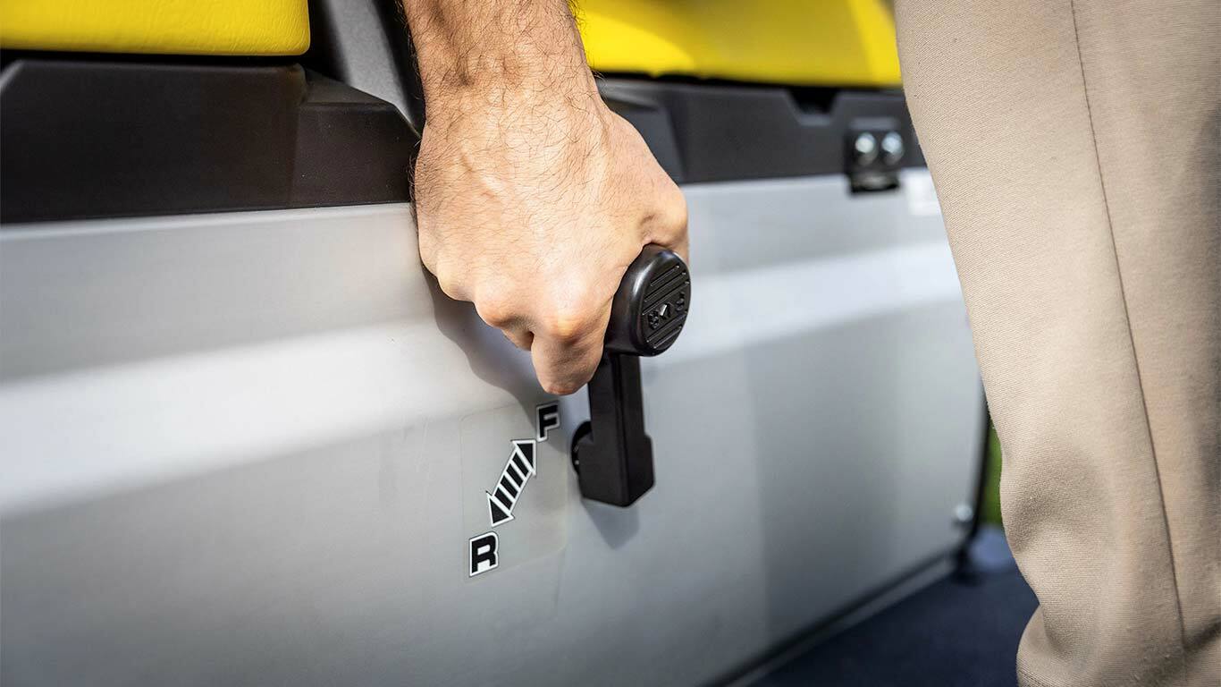 תקריב של יד מושכת את ידית ההילוכים ב-John Deere Gator GS, עם הילוך קדימה ואחורה ליד המושבים הצהובים.