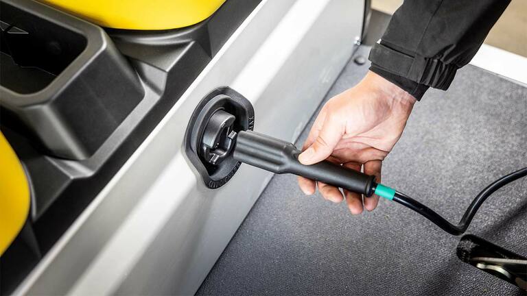 יד מחברת את כבל הטעינה לפתח הצדי ברכב ייעודי John Deere Gator GS חשמלי.