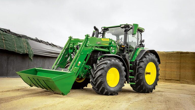 טרקטור John Deere עם מעמיס קדמי חונה בחווה בסמוך לאחסון תחמיץ.